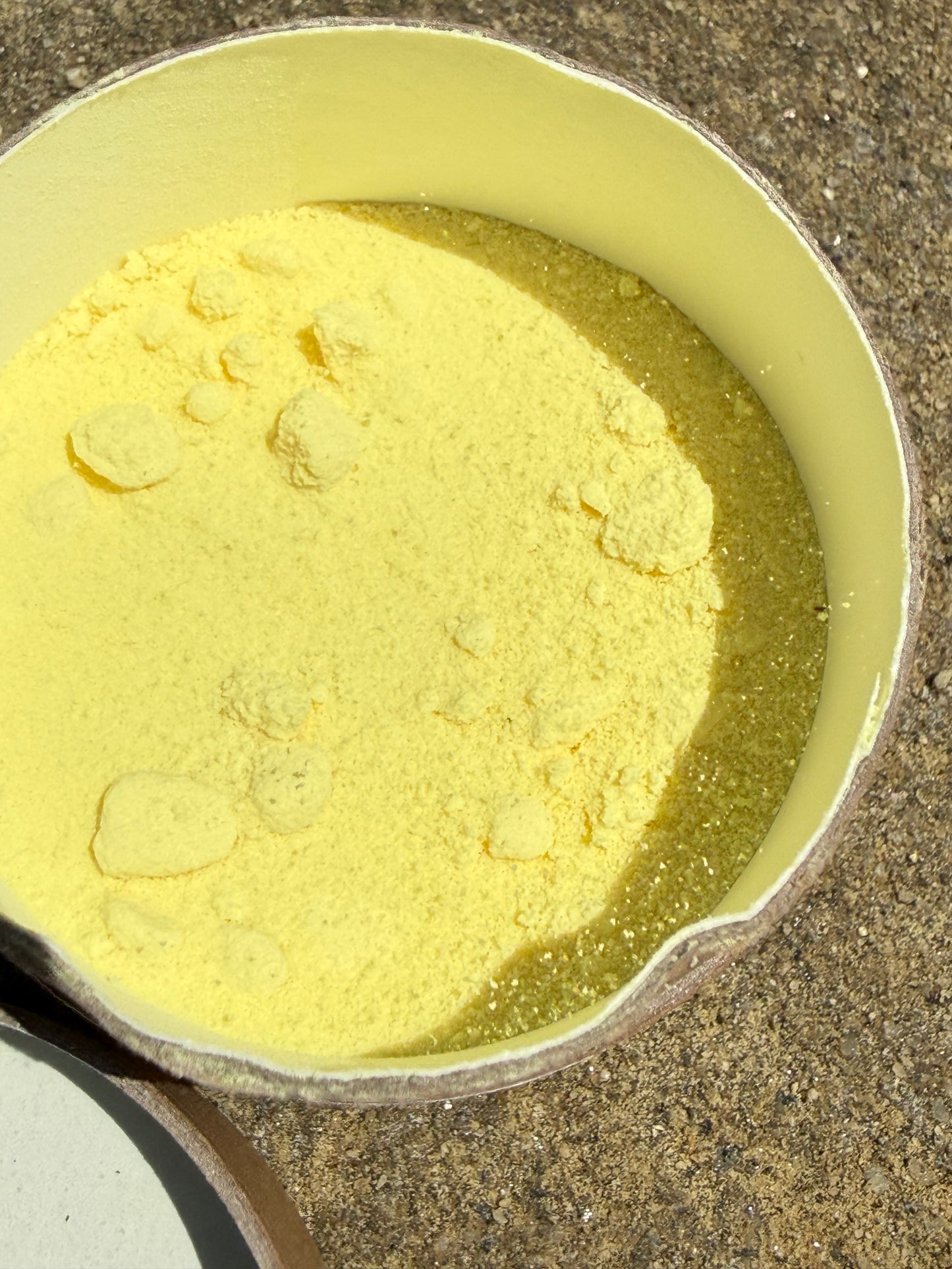 A close-up of a light yellow powder, likely cornstarch or flour, sitting in a shallow dish on a textured concrete surface.